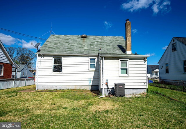 rear view of house featuring central air condition unit, a chimney, fence, and a lawn