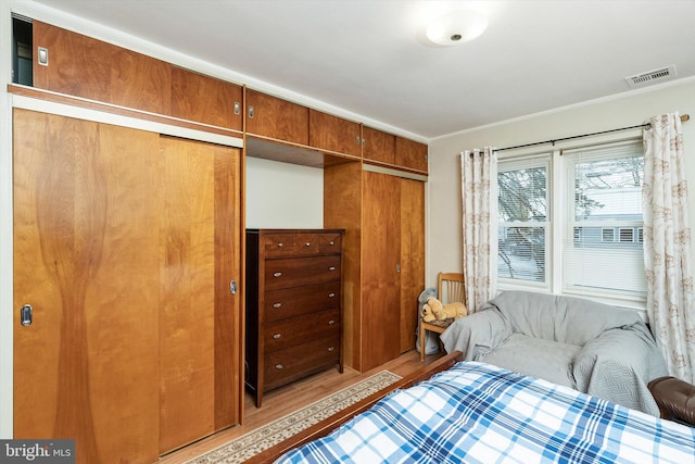 bedroom featuring visible vents, a closet, crown molding, and light wood-style flooring