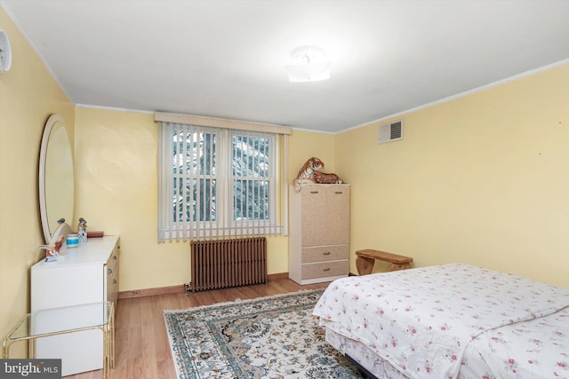 bedroom featuring baseboards, ornamental molding, radiator heating unit, visible vents, and light wood finished floors