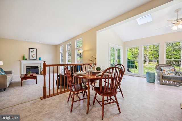 dining area with a ceiling fan, a glass covered fireplace, a healthy amount of sunlight, and vaulted ceiling with skylight