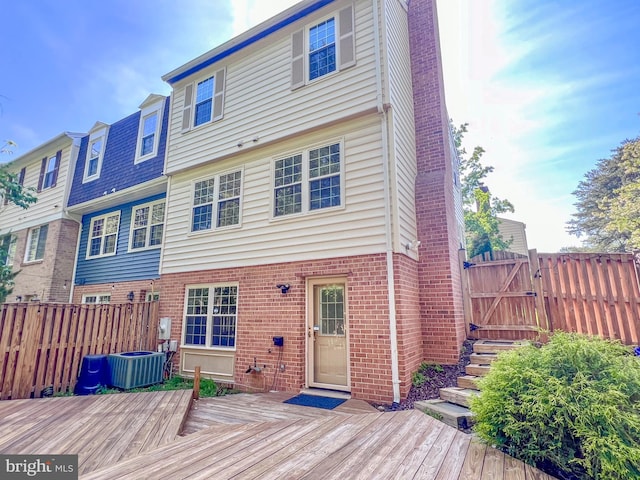 rear view of house featuring brick siding, central AC unit, a wooden deck, and fence