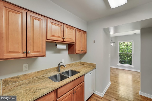 kitchen featuring light wood-type flooring, dishwasher, a sink, baseboards, and light stone counters