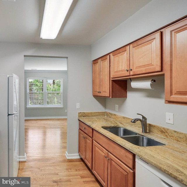 kitchen with white appliances, baseboards, light stone counters, a sink, and light wood finished floors