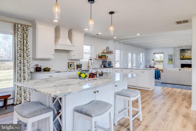 901 Riverside Ave, Grottoes, VA 24441 - kitchen with premium range hood, white cabinets, a kitchen island with sink, visible vents, and light wood finished floors
