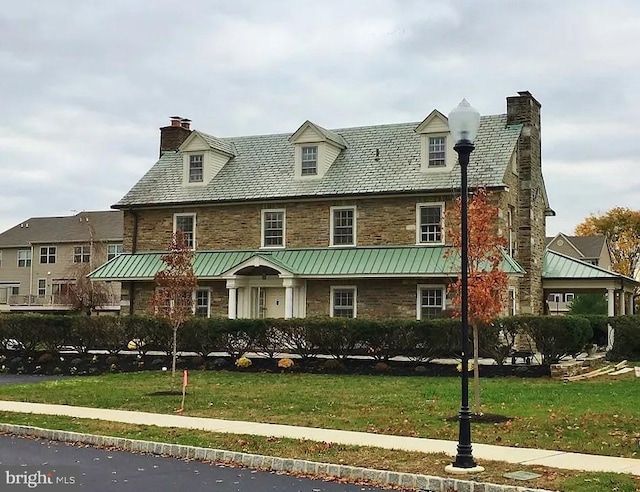 cape cod house featuring a front yard, a high end roof, stone siding, and a chimney