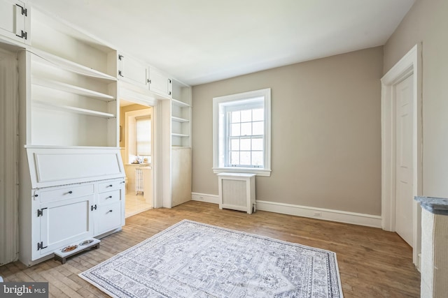 unfurnished bedroom featuring ensuite bath, light wood-type flooring, baseboards, and radiator