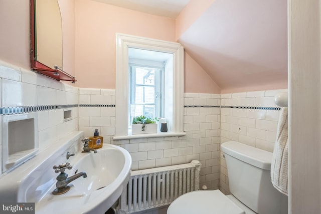 half bathroom featuring radiator heating unit, vaulted ceiling, toilet, a sink, and tile walls