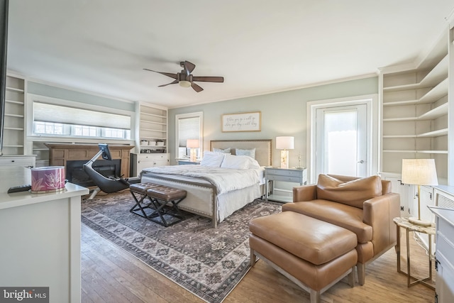 bedroom with multiple windows, wood finished floors, and a glass covered fireplace