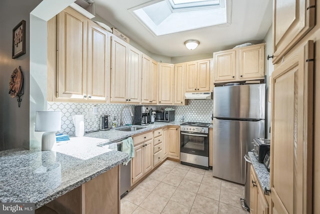 kitchen with light brown cabinets, a sink, under cabinet range hood, stainless steel appliances, and a skylight