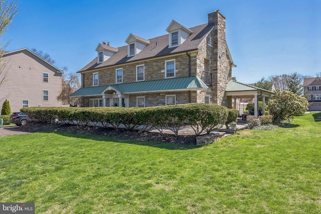 view of front of property with a chimney, stone siding, a front yard, a standing seam roof, and metal roof
