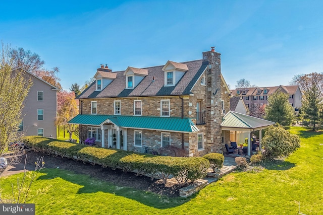 back of house featuring a chimney, stone siding, and a yard
