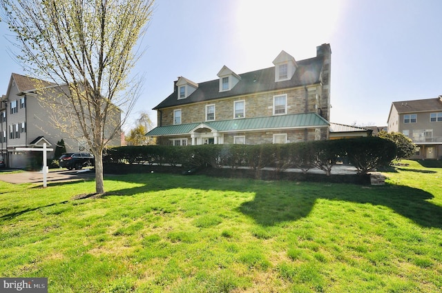 exterior space with a front lawn, stone siding, metal roof, and a chimney