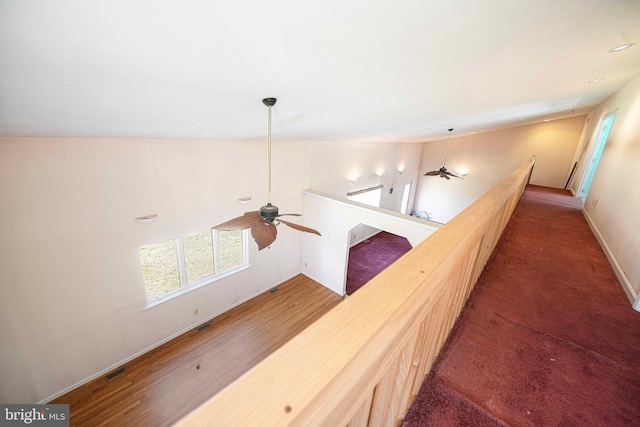 hallway with an upstairs landing, baseboards, wood finished floors, and visible vents