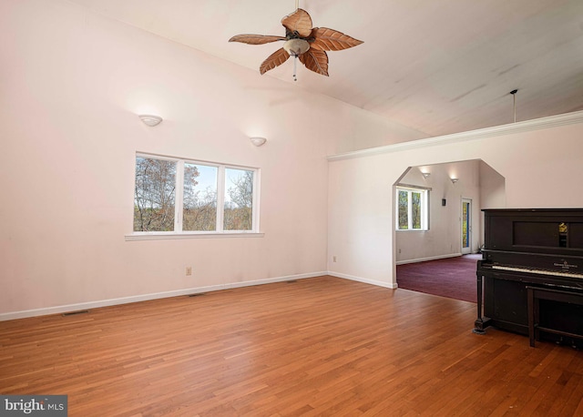 unfurnished living room featuring a ceiling fan, wood finished floors, arched walkways, baseboards, and lofted ceiling