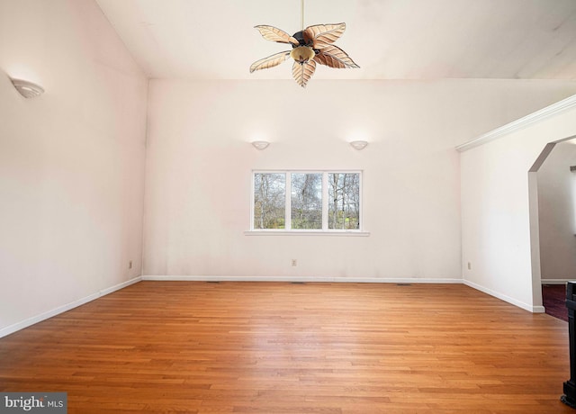 spare room featuring arched walkways, light wood-style floors, a ceiling fan, and baseboards
