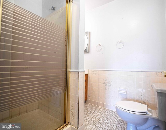 bathroom featuring toilet, tile walls, wainscoting, a stall shower, and tile patterned flooring