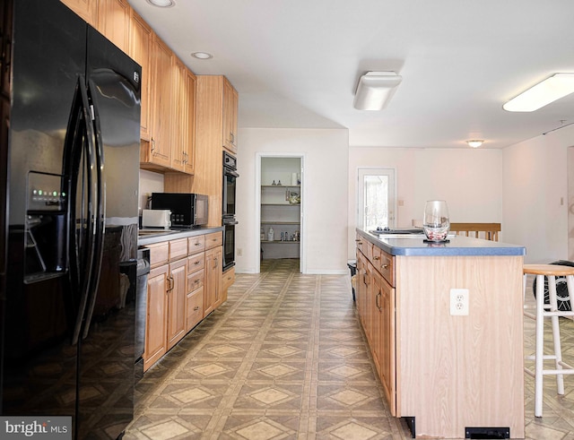 kitchen featuring a breakfast bar, light brown cabinetry, black appliances, and a center island with sink