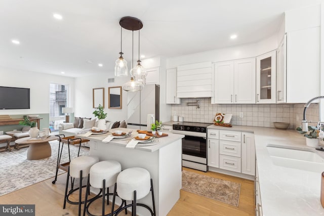 kitchen featuring a kitchen bar, white cabinets, light countertops, a sink, and electric range oven