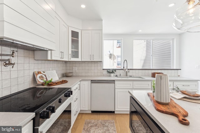 kitchen featuring dishwasher, a sink, white cabinetry, backsplash, and light wood-style flooring