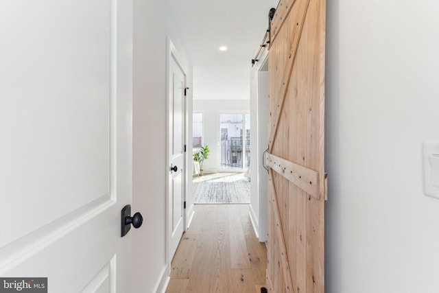 hall featuring recessed lighting, a barn door, baseboards, and light wood finished floors
