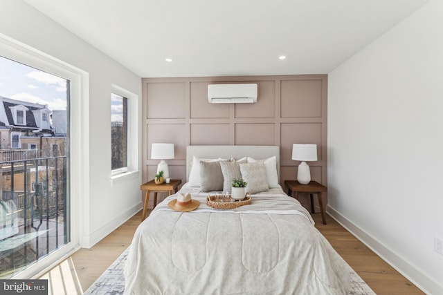 bedroom featuring a wall mounted AC, baseboards, recessed lighting, a decorative wall, and light wood finished floors