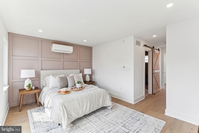 bedroom with light wood-style floors, a decorative wall, visible vents, a barn door, and a wall mounted air conditioner
