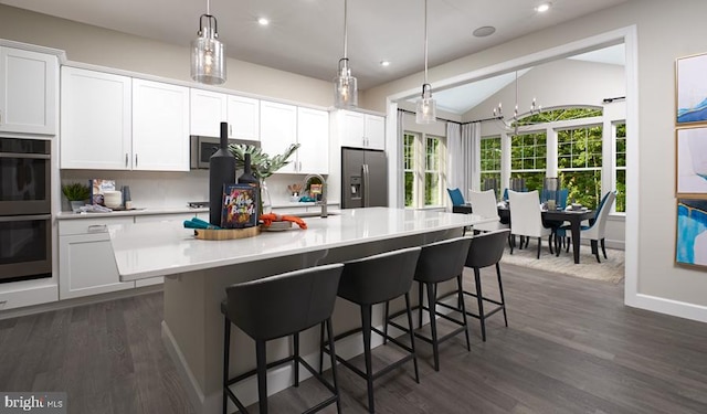 kitchen featuring stainless steel fridge with ice dispenser, recessed lighting, an island with sink, dark wood-style floors, and double oven