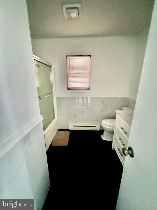 1076 Lancaster Dr, Bushkill, PA 18324 - bathroom featuring combined bath / shower with glass door, a baseboard heating unit, toilet, a wainscoted wall, and tile walls
