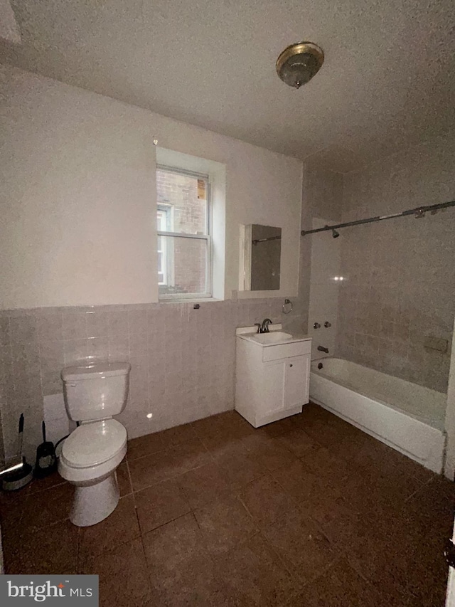 bathroom with toilet, tile walls,  shower combination, vanity, and a wainscoted wall