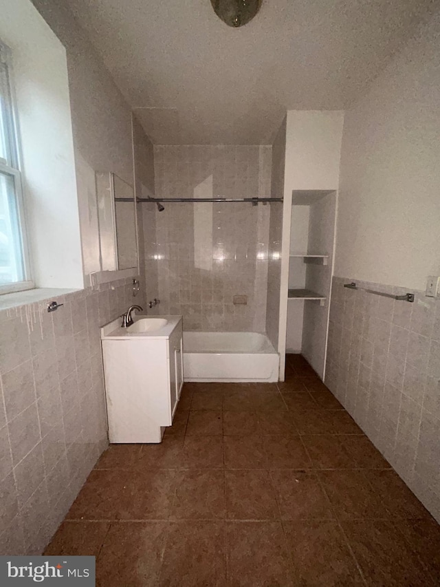 full bath with tile walls, vanity, a wainscoted wall, tile patterned flooring, and bathing tub / shower combination