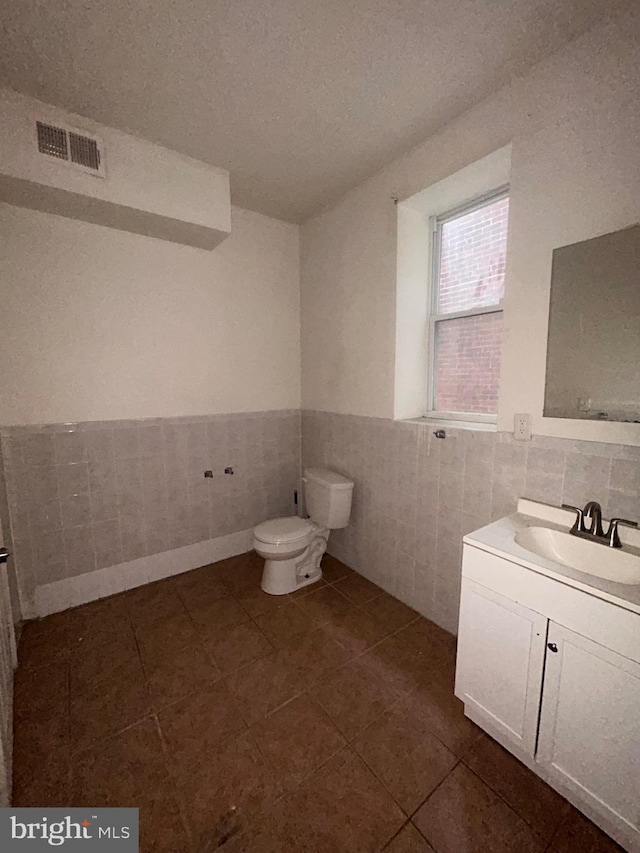 bathroom featuring vanity, visible vents, a wainscoted wall, toilet, and tile walls