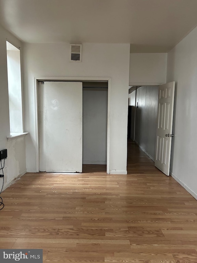 unfurnished bedroom featuring visible vents, a closet, baseboards, and wood finished floors