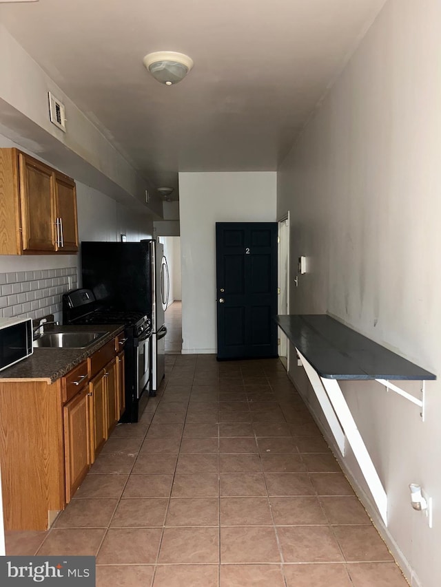 kitchen featuring tasteful backsplash, light tile patterned flooring, dark countertops, stainless steel gas stove, and a sink