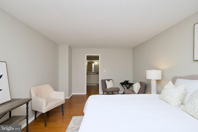bedroom with baseboards, wood finished floors, and connected bathroom
