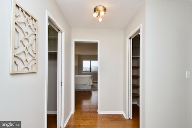 hall with baseboards, a textured ceiling, and wood finished floors