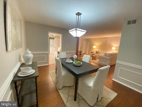 dining area with wainscoting, a decorative wall, dark wood finished floors, and visible vents