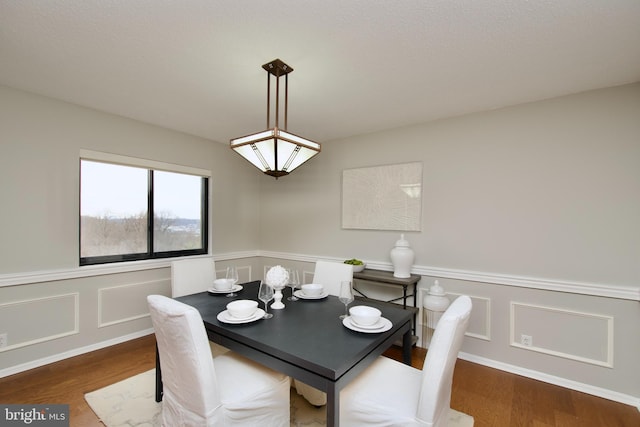 dining room featuring wainscoting, a decorative wall, and wood finished floors