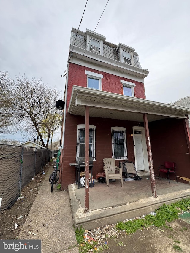 view of front facade featuring covered porch, brick siding, mansard roof, and fence