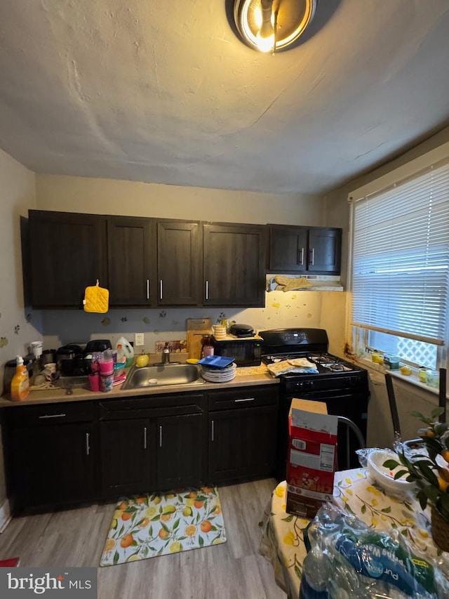 kitchen with black gas stove, a sink, light countertops, light wood finished floors, and under cabinet range hood