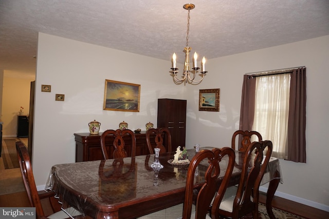 dining space featuring a textured ceiling, wood finished floors, a notable chandelier, and baseboards