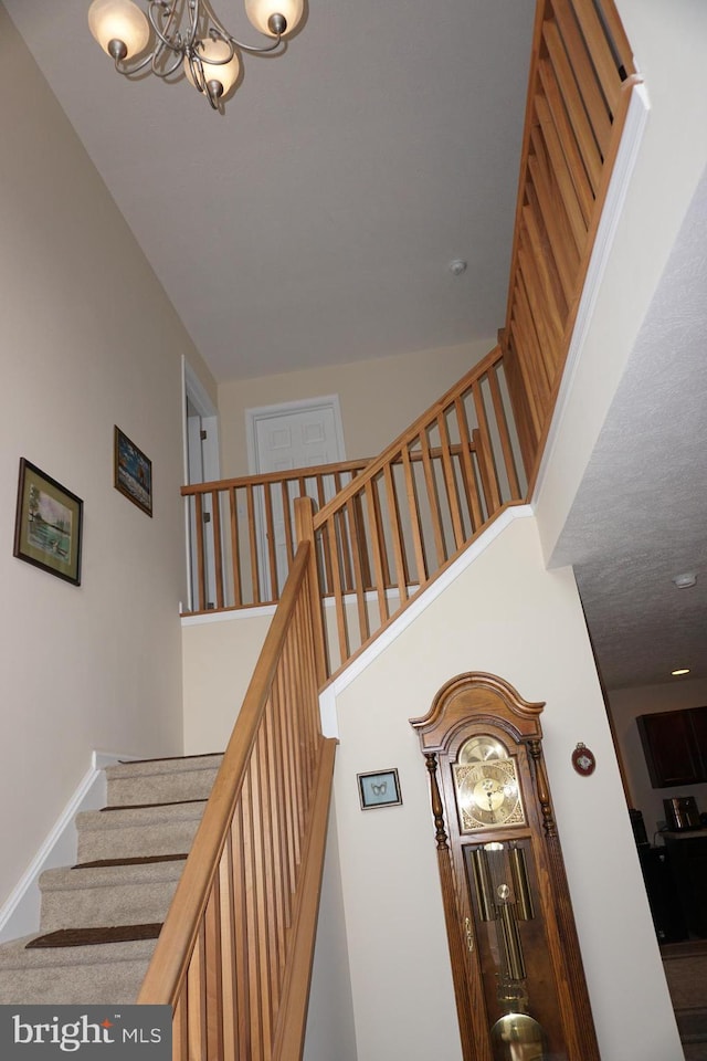 staircase with a high ceiling, a notable chandelier, and baseboards