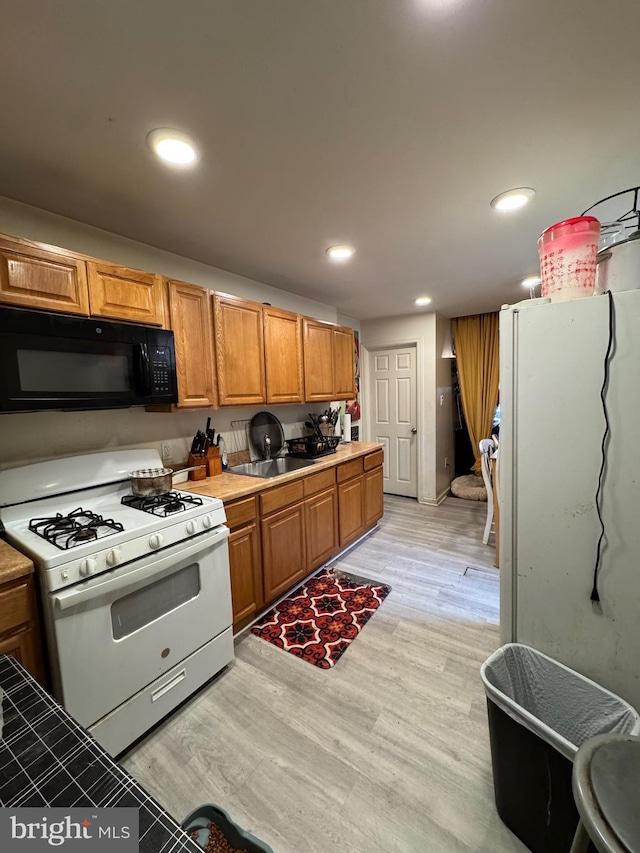 kitchen featuring brown cabinetry, black microwave, white gas stove, recessed lighting, and light wood finished floors