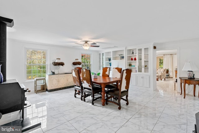 dining space with a wood stove, marble finish floor, a ceiling fan, and ornamental molding