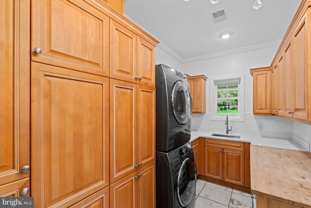 washroom featuring ornamental molding, light tile patterned floors, stacked washer / dryer, cabinet space, and a sink