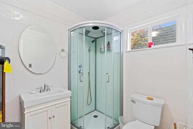 bathroom with a shower stall, toilet, vanity, and tile walls