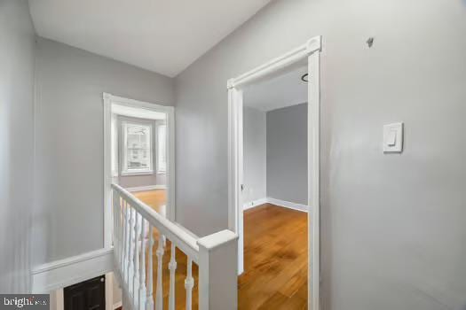 hall with baseboards, an upstairs landing, and wood finished floors