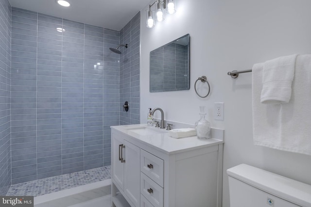 bathroom featuring toilet, tiled shower, and vanity
