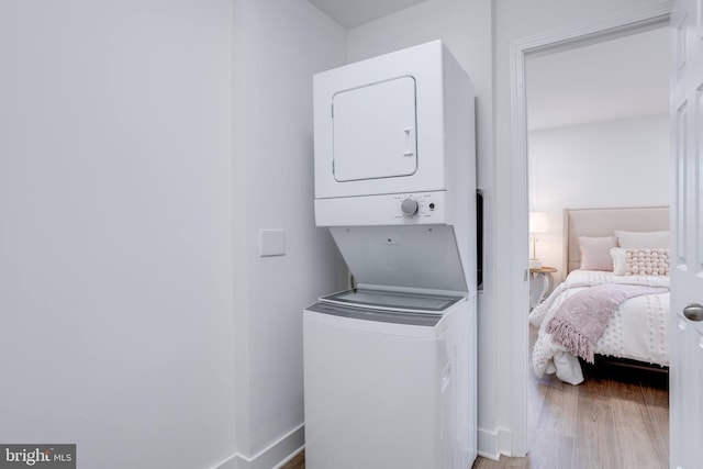 laundry room featuring baseboards, wood finished floors, stacked washer / dryer, and laundry area
