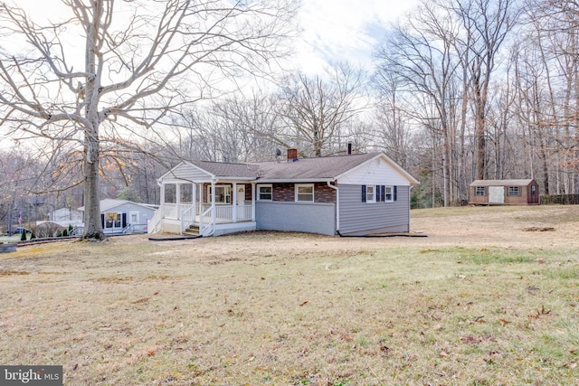 view of front of property with a chimney, a front yard, brick siding, an outbuilding, and covered porch