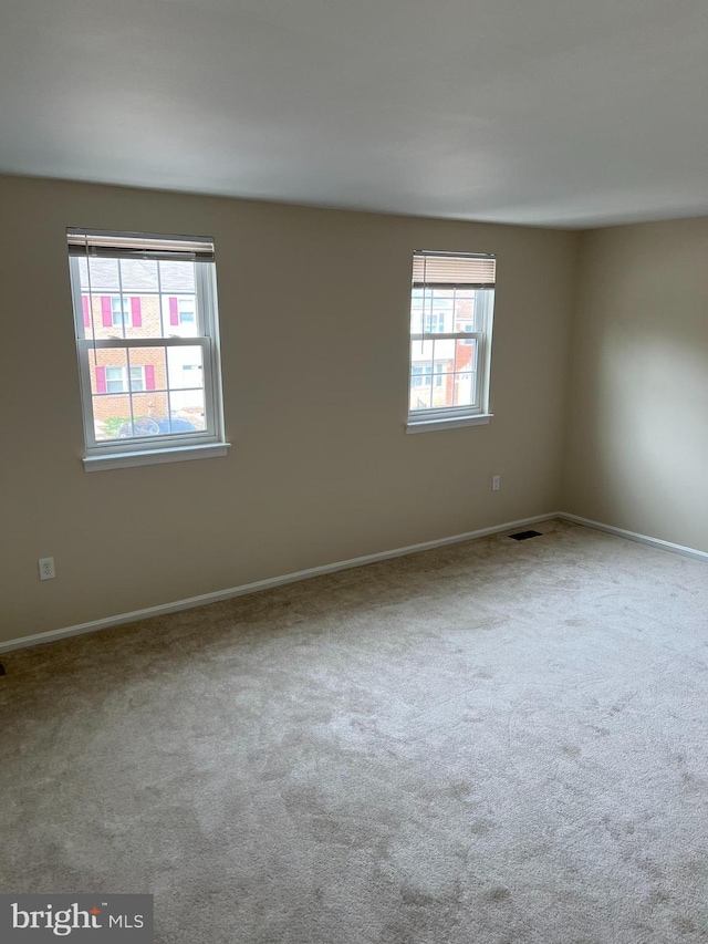carpeted spare room featuring visible vents and a healthy amount of sunlight